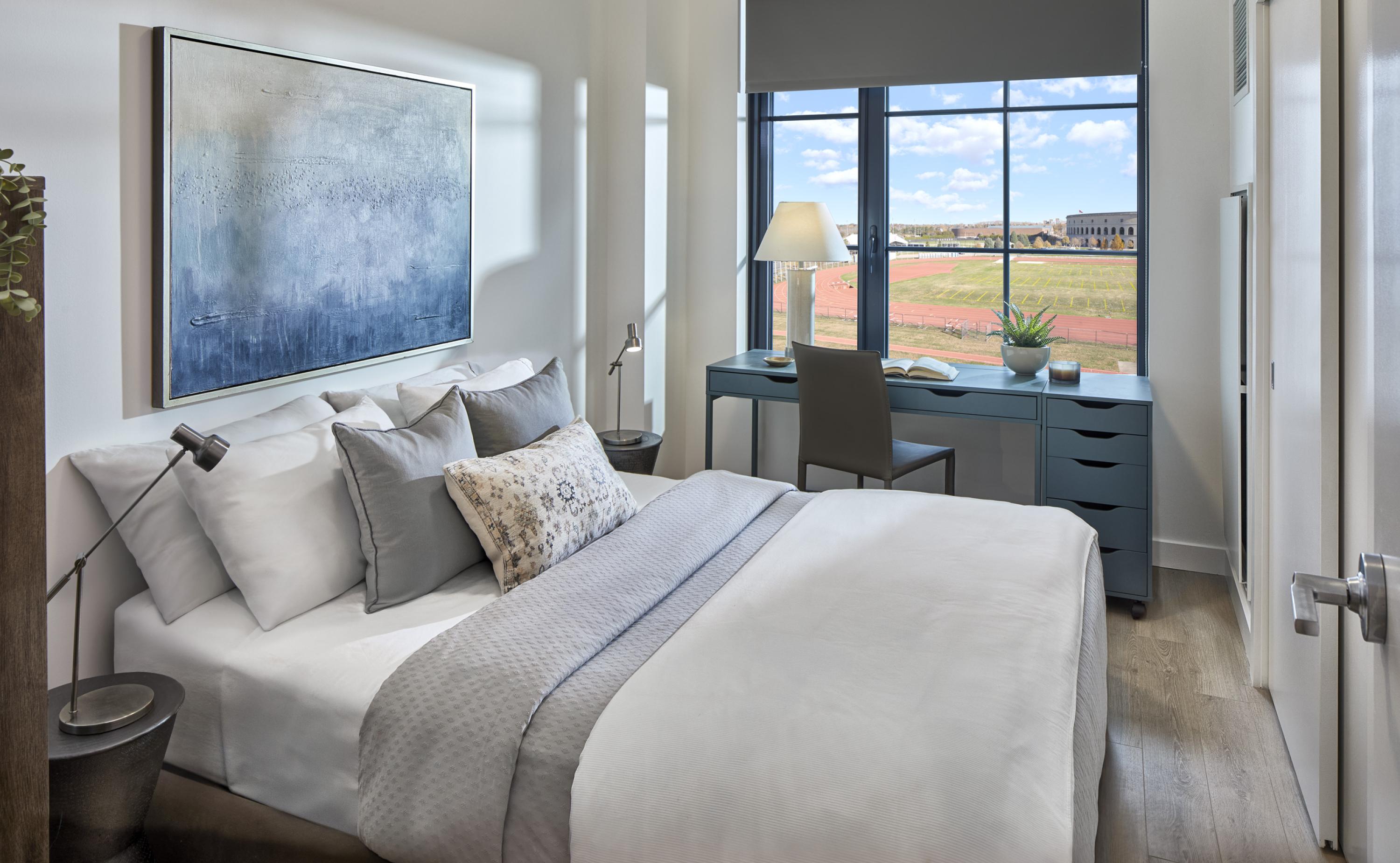 Bedroom mock unit with hard flooring, sliding closet doors, and a view of the athletic fields