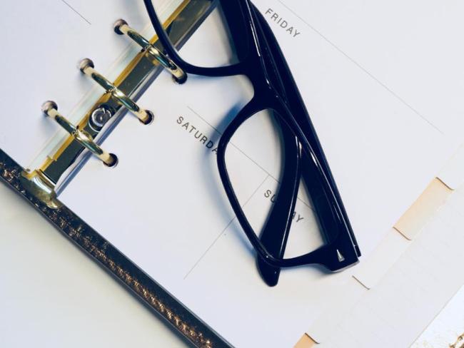 A calendar planner sitting open face up on a table with a pair of glasses resting on top