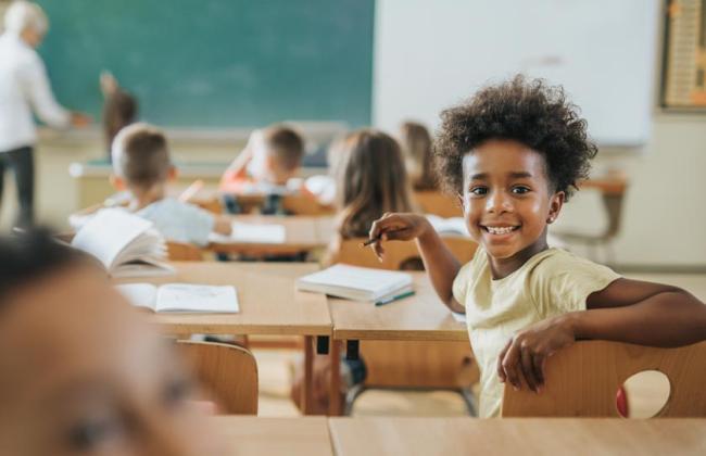 An elementary school student sitting at their desk and smiling in class