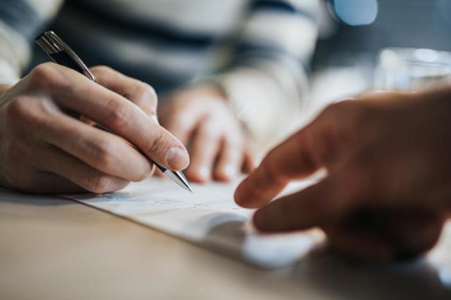 Close up of a man signing a contract while financial advisor is aiming at the place he need to sign.