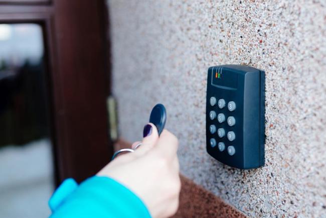Woman holding a key fob up to a key pad to unlock the door to the house.