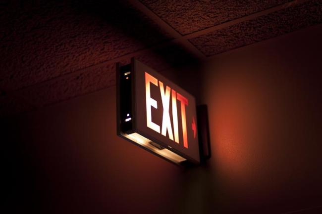 A red exit sign that is illuminated in a dark hallway.