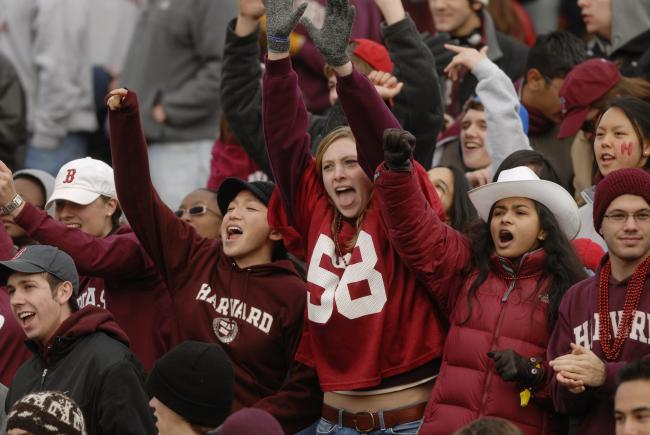 A group of Harvard students in the stands, cheering during an athletics game. 