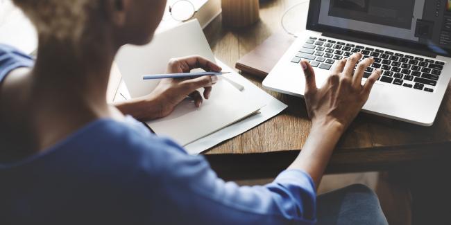 someone browsing their computer, with a pen and paper in hand.