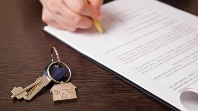 someone signing a document, with keys in focus on the table