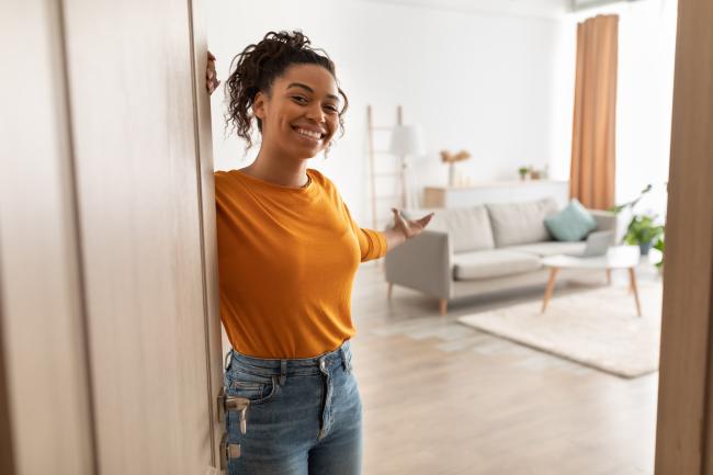 a girl warmly welcoming someone into her apartment, holding open the door and motioning them in