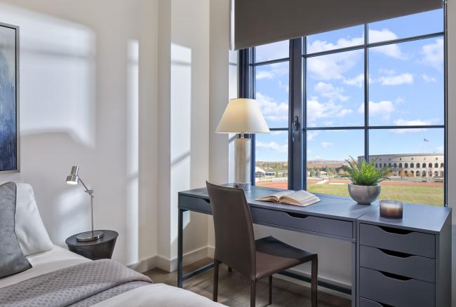 Bedroom mock unit with hard flooring and large bright windows with a view of the athletic fields