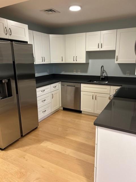 Kitchen with dark countertops and wood floors, stainless steel appliances and white cabinetry