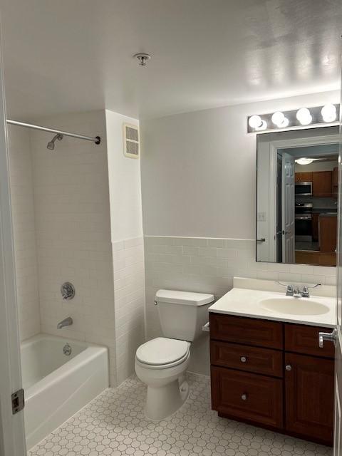 Primary bathroom with tub + shower, white tile flooring, toilet, and a vanity with sink and lower cabinetry