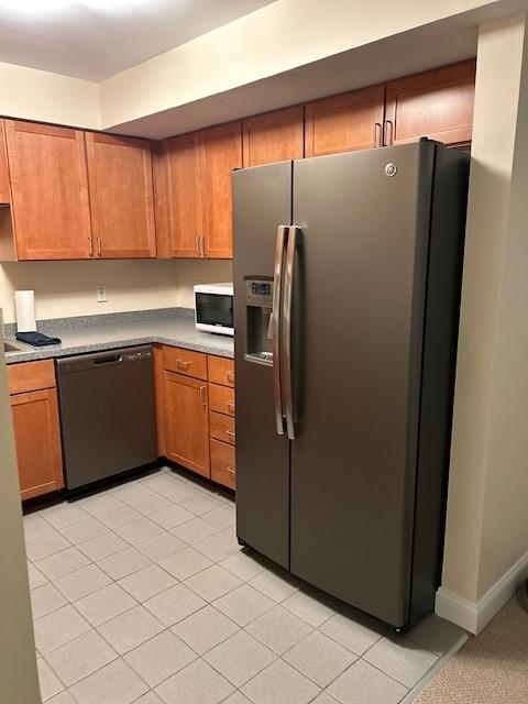 Kitchen with wood cabinetry, grey countertops, and stainless steel appliances. Floor is tiled.