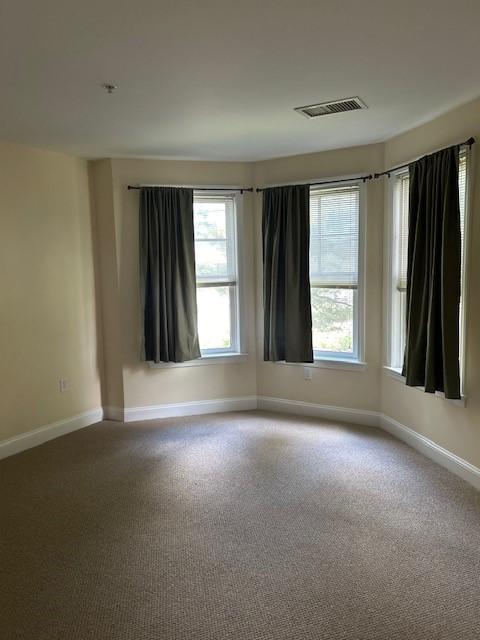 A room with carpet, and large bay windows with curtains.