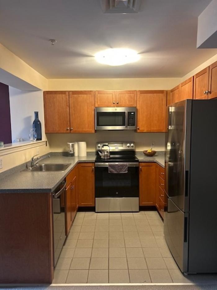 Kitchen with stainless steel appliances, wood cabinetry, overhead lighting, and tile floor.