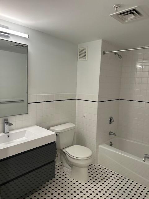 secondary bathroom with white tiling, vanity with mirror, shower/tub, and toilet