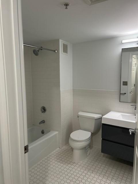 Primary bathroom with white tiling, vanity with mirror, shower/tub, and toilet