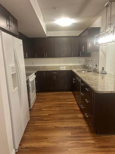 Kitchen with white appliances, hard flooring, dark cabinetry, and light countertops